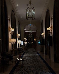 an elegant hallway with chandeliers and lamps on either side of the corridor is lit up