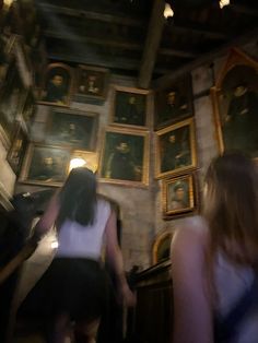 two women are walking up the stairs in front of paintings on the wall behind them