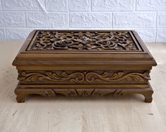 an intricately carved wooden box sitting on top of a wood table next to a brick wall