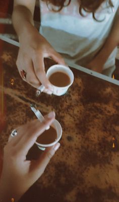 two hands holding cups of coffee on top of a table