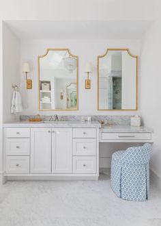 a white bathroom with two mirrors and a blue chair in front of the vanity area