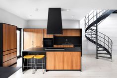 a kitchen with black counter tops and yellow stools next to a spiral stair case