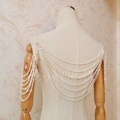 a white mannequin with pearls on it's neck and back, sitting in front of a wall