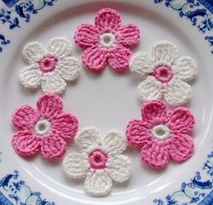 pink and white crocheted flowers are on a blue and white plate with floral designs