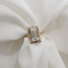 a diamond ring sitting on top of a white satin material with a large emerald stone surrounded by smaller diamonds