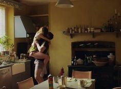 two people hugging in the kitchen next to a table