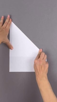 two hands holding up a piece of white paper on top of a gray surface with one hand reaching for it