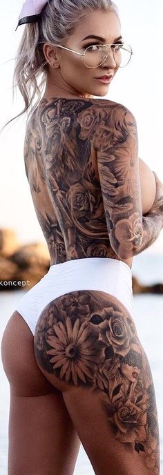 a woman with tattoos on her back standing next to the ocean