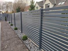 a grey fence with gravel and rocks in front of it, next to a house