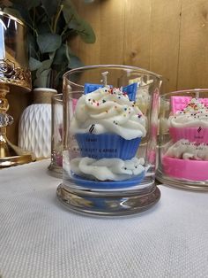 three cupcakes with white frosting and sprinkles are in glass cups on a table