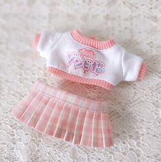 a pink and white doll outfit is laying on a lace tablecloth