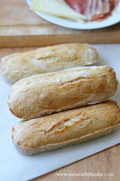 three baguettes sitting on top of a cutting board next to a plate with meat