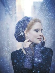 a woman wearing a hat and scarf in the snow with her hands on her face