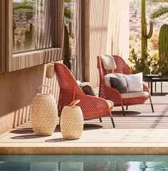 three chairs and two vases sitting on the side of a pool next to a house