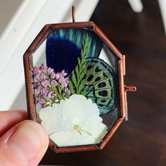 a hand holding an ornament with flowers and a butterfly on the inside of it