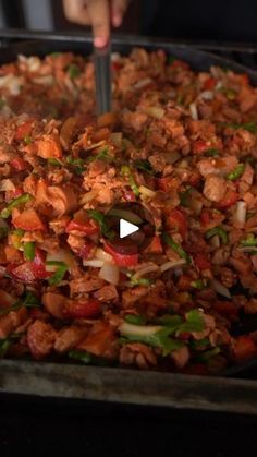 a pan filled with meat and veggies on top of a table next to a person