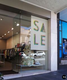 a store front with the words sale written on it's glass display window and cars parked outside