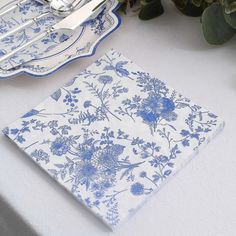 a blue and white place setting with silverware on the table, next to a bouquet of flowers