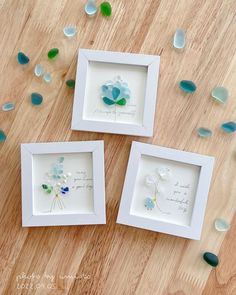 three framed pictures with sea glass in them on a wooden table next to some flowers