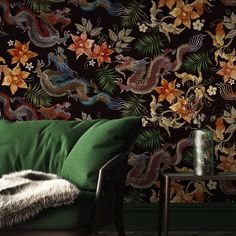 a green couch sitting in front of a wall covered in flowers and dragon design on it