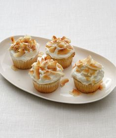 four cupcakes with white frosting and toasted almonds on a plate