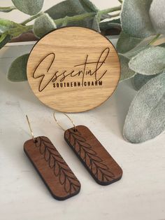 two wooden earrings with the words essential written on them next to some leaves and a plant