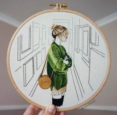 a woman in green is holding a purse and cross - stitching on a hoop