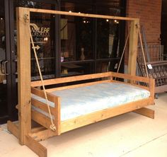 a wooden swing bed sitting on top of a sidewalk next to a store front door