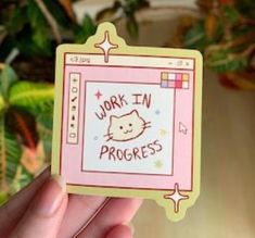 a person holding up a sticker that says work in progress with a cat on it