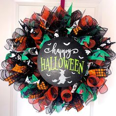 a halloween wreath hanging on the front door decorated with black and orange mesh, green and red decorations