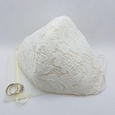 two wedding rings are laying next to a lace covered pillow and ring holder on a white background