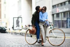 a man and woman riding on the back of a bike down a cobblestone street