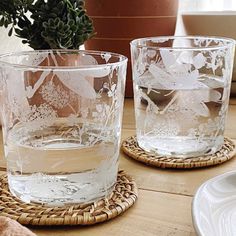 two clear glasses sitting on top of a wooden table next to a potted plant