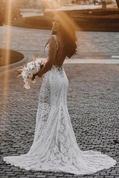 a woman in a wedding dress standing on a brick road with the sun behind her