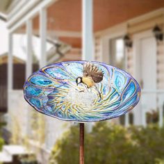 a bird is sitting on top of a glass bowl in front of a house with trees and bushes