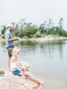 a man and woman fishing with their dog on the rocks by the water's edge