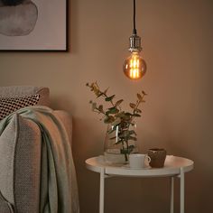 a white table with a vase and some flowers on it next to a light bulb