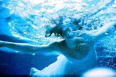 a woman in white dress under water with blue light coming from her face and arms