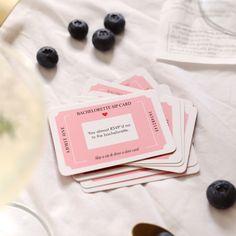 three pink and white cards with blueberries on them next to some wine glasses