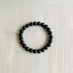 "DETAILS:  8mm Matte Black Onyx beaded bracelet on clear elastic stretch cord. A smooth matte finish gives the bracelet a sleek modern look. It is a unisex bracelet making it a good choice for men, women, and teens.  SIZE: Add .75\" - 1.0\" inch to your wrist measurement.  DESCRIPTION: Whether you are looking for a statement piece or a subtle addition to your collection, this bracelet is a great choice. It is a minimalist-style unisex stretch bracelet making it a good choice for men, women, and Classic Black Beaded Bracelets As Gift, Minimalist Black Onyx Beaded Bracelets, Classic Black Onyx Bracelets, Classic Black Onyx Bracelet, Classic Black Bracelets With 8mm Beads, Minimalist Onyx Beaded Bracelets With Round Beads, Classic Black Beaded Bracelets For Everyday, Minimalist Onyx Beaded Bracelet With Round Beads, Classic Black Beaded Bracelets