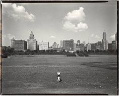 black and white photograph of a person in a field with buildings in the background,