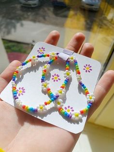 a hand holding a small beaded necklace with flowers on it's end and a white card attached to the back