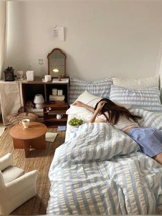 a woman laying in bed on top of a blue and white comforter next to a coffee table