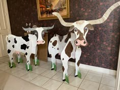 three paper cows are standing in front of a wall with a painting on the wall behind them