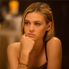 a beautiful young blonde woman sitting at a table with her hand on her chin and looking off to the side