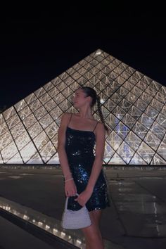 a woman standing in front of the pyramid at night with her hand on her hip