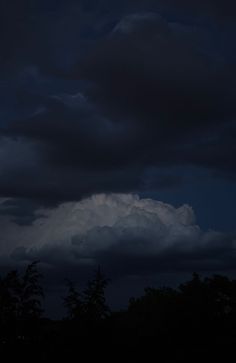 an airplane is flying in the sky with dark clouds behind it and some trees below