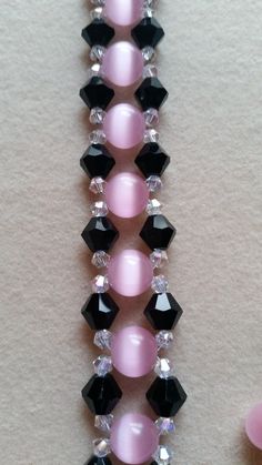 a pink beaded necklace with black and white beads on it's side, next to a pair of scissors