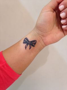 a small black bow tattoo on the wrist