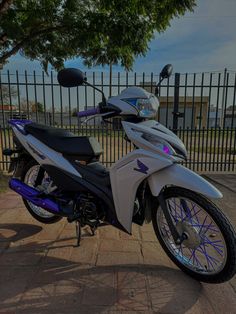 a motorcycle parked next to a fence on a brick sidewalk in front of a tree